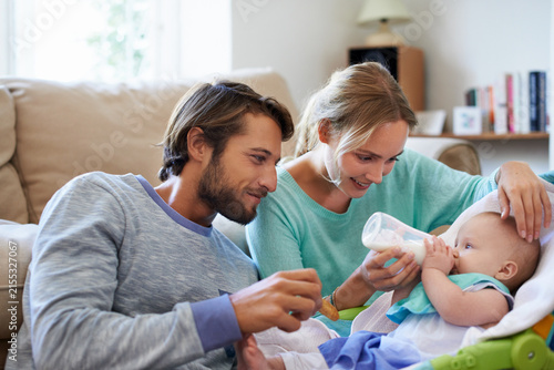Mom, dad and feeding with baby bottle for wellness, development or nutrition with foster child. Milk, happy family or infant kid on rocker with formula drink, growth or adoption with parents in home