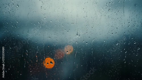 Close up of raindrops on a window pane with warm orange bokeh lights at dusk.