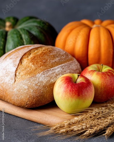 Colorful display of bread, pumpkins, apples, and wheat on a wooden board in a kitchen setting. Sourdough September
