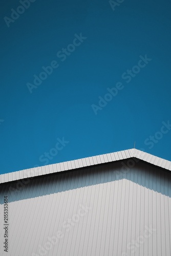 Minimalist geometric composition of a stark white corrugated metal roof against a vibrant, clear blue sky on a bright day