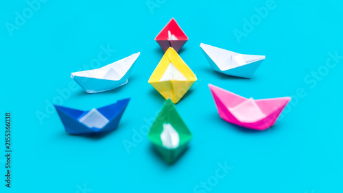 Foto Group of colorful origami paper boats facing a yellow leader boat on a blue background