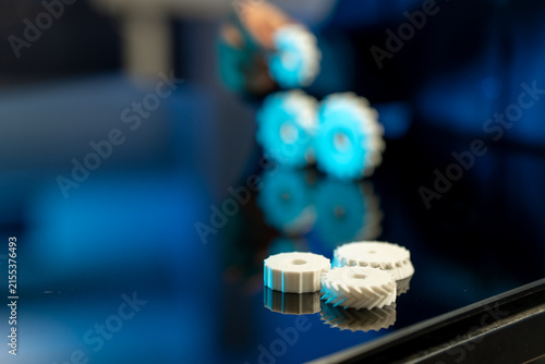Small white plastic gears on a glossy surface with blurred machinery in blue light