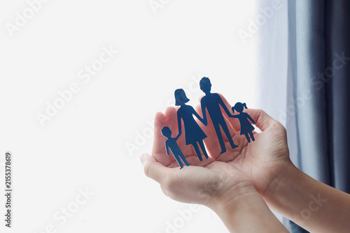 Close-up of hands holding paper cutout of family near window. Concept of family insurance, protection, care, and security.