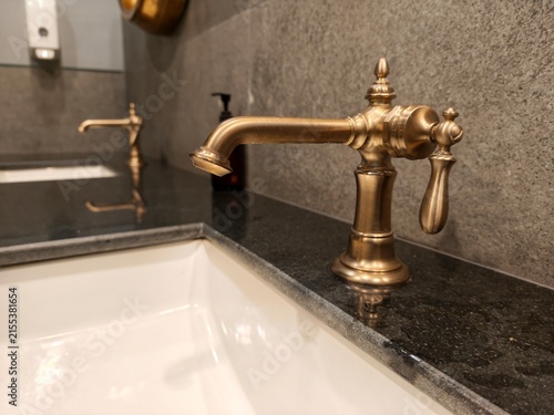 фотографія A close-up shot of an elegant vintage brass faucet mounted on a black granite countertop with a white undermount sink in a luxurious modern bathroom