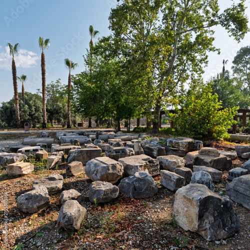 Ancient marble architectural fragments from Hadrian's Arch displayed at the Perge archaeological site in Antalya, Turkey with palm trees in the background