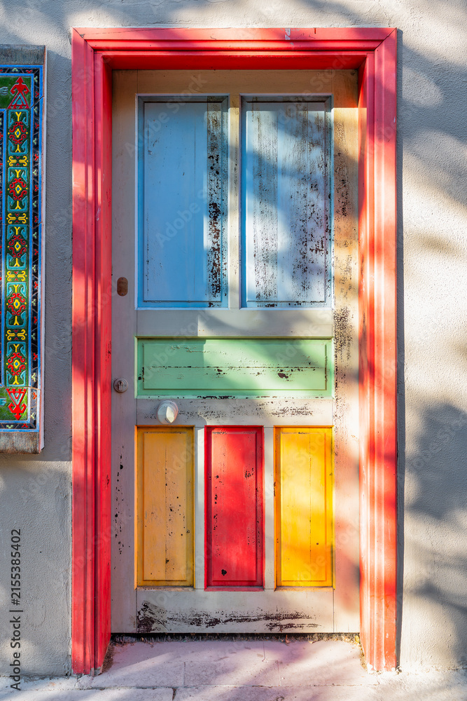 Fototapeta premium Colorful rustic wooden door with traditional tiles in the historic Kaleici district of Antalya, Turkey, featuring a vibrant red frame and distressed multi-colored panels on an old house facade