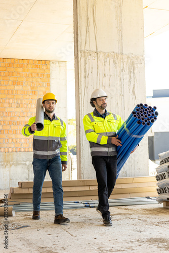 Two diverse construction workers carrying pipeline and pipe
