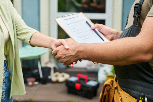 Caucasian male technician shaking hands with female client holding clipboard outdoors, representing successful home repair service agreement, suitable for local business marketing