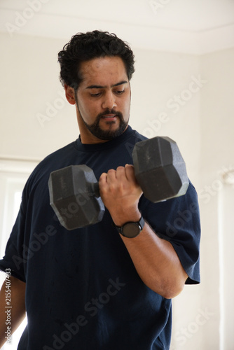 Foto Mid-adult African American man curling hexagonal dumbbell at home, wearing navy