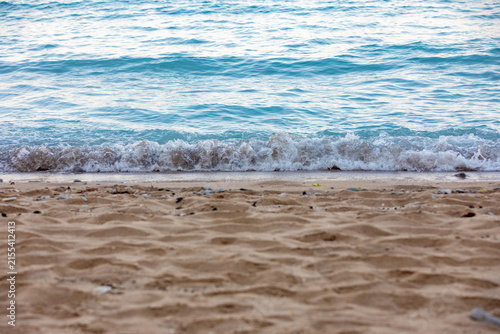 Fotografie Close-up of gentle waves rolling onto a sandy beach with clear blue water, perfect for summer, relaxation, and travel themes