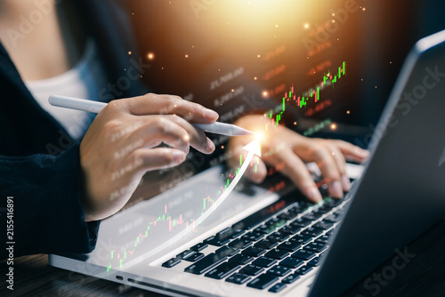 Financial analyst using laptop and digital pen with rising stock market chart, illustrating investment growth, trading strategy, market analysis, finance technology, and business profit.