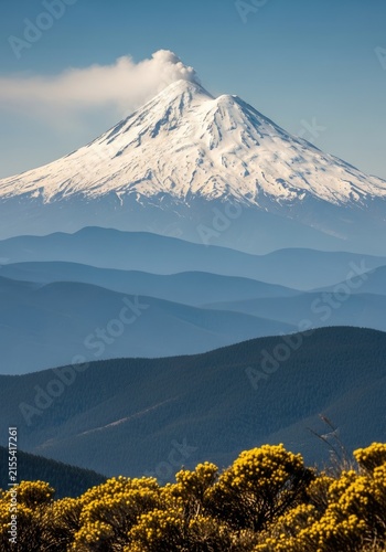 Majestic Snow-Capped Volcano Towering Over Lush Green Hills and Blue Sky.