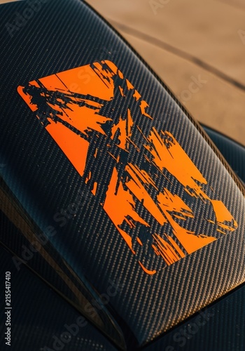 Close-up of a vibrant orange graphic of a race car on a dark carbon fiber surface.