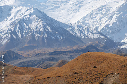 Canvastavla Small figures of hikers walking on mountain ridge with majestic snow-capped Leni