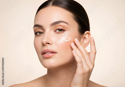 Beautiful woman applying liquid foundation cream to her glowing face
