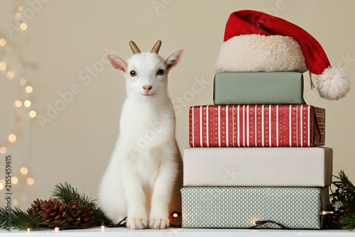 White rabbit beside stacked gift boxes with a Santa hat in a festive holiday setting, cozy seasonal concept, Christmas, New Year.