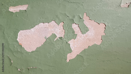 Close up of an aged wall where light green paint is peeling away to reveal pink orange plaster beneath, showing cracks, bubbles, and textured wear accumulated over time.