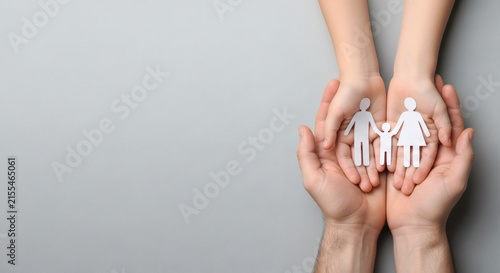 Health and life insurance concept with child and adult hands holding white paper family cutout.