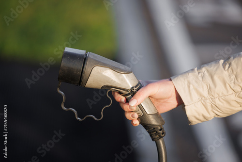 Woman holding an electric vehicle charging connector for a modern automobile, representing sustainable transportation, clean energy, battery technology and the transition toward electric mobility