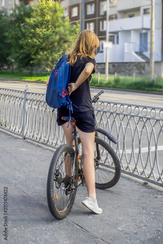 A woman with a bicycle stopped on the sidewalk on a summer day