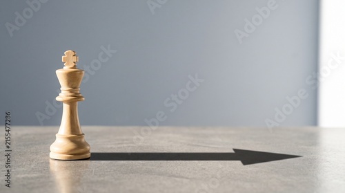 White chess king casting dramatic shadow arrow on reflective surface in minimalist setting