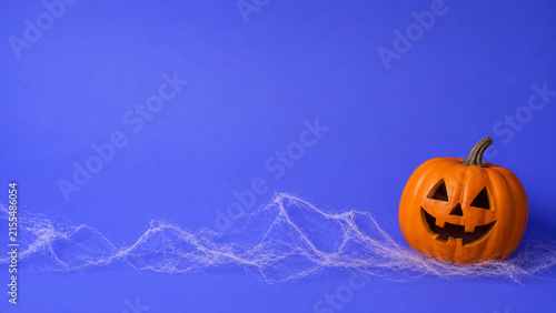 Jack-o-lantern pumpkin on cobweb against blue background. Halloween celebration and spooky decoration concept. Horizontal view with copy space
