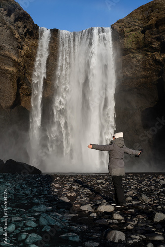 Fotografía Woman Standing with Open Arms facing Skógafoss Waterfall in Iceland