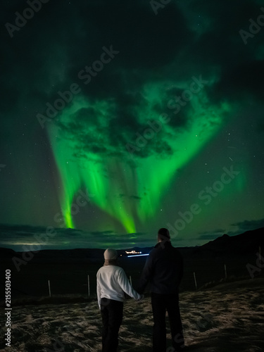 Couple in Winter Gear Holding Hands Under Vertical Aurora Borealis
