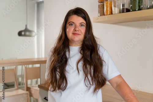 Beautiful Caucasian woman in white t-shirt and with curly hair smiling in kitchen