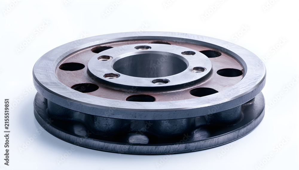 Obraz premium Heavy industrial steel flywheel rests on white background. Solid metal engine component features round circular shape with machined surface texture. Precise iron gear part provides mechanical energy