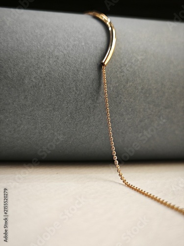 Vertical close-up of a delicate gold necklace. Minimalist curved bar pendant on a grey cylinder
