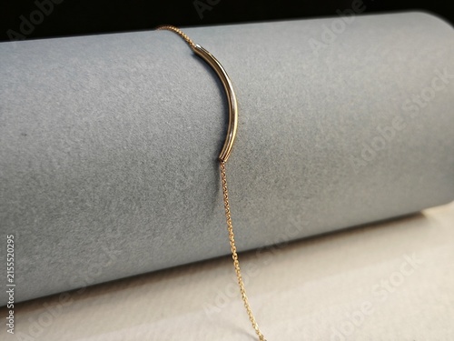 Minimalist gold necklace with a curved bar pendant. Elegant fine chain jewelry on a grey display