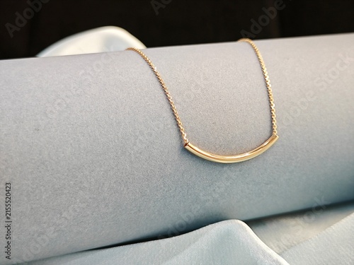 Delicate gold curved bar necklace on a grey cylinder and blue satin. Minimalist elegant jewelry