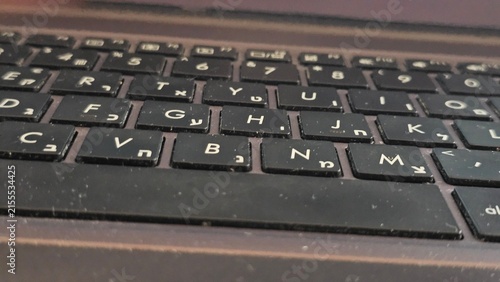 Obraz na płótnie A close-up macro shot of a dusty black laptop keyboard with bilingual Latin and Hebrew character keycaps