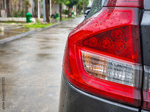 Wet Modern Car Taillight Detail. Close-up of a sleek red automobile rear light covered in fresh raindrops on a rainy street.