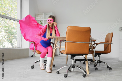 Obraz na płótnie Young woman in superhero costume and pink mask sitting at an office desk, busine