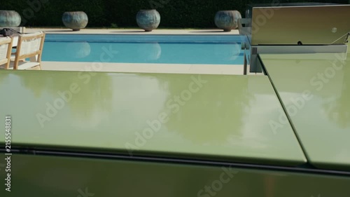 Modern green outdoor kitchen overlooks a tranquil pool and lush garden