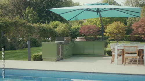 Luxury outdoor kitchen with umbrella near swimming pool and lush greenery