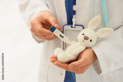 Male pediatrician with toy bunny and thermometer in clinic, closeup
