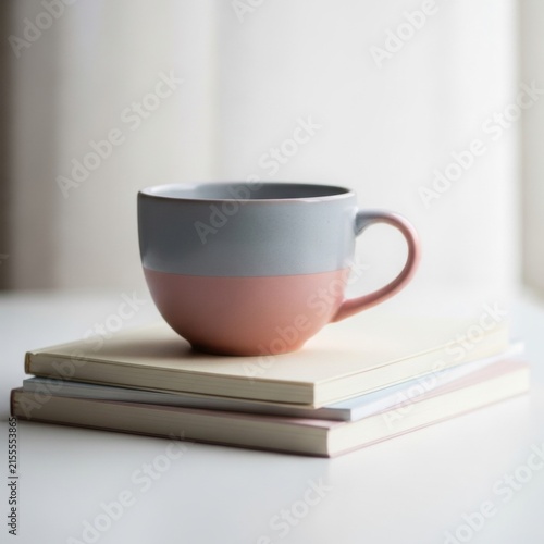 A ceramic coffee mug with pink and grey paint sitting on a stack of books