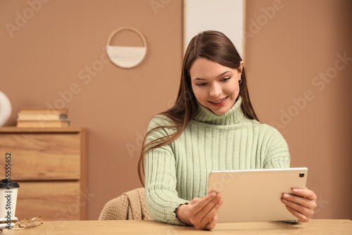 Beautiful young woman with modern tablet computer at table in room