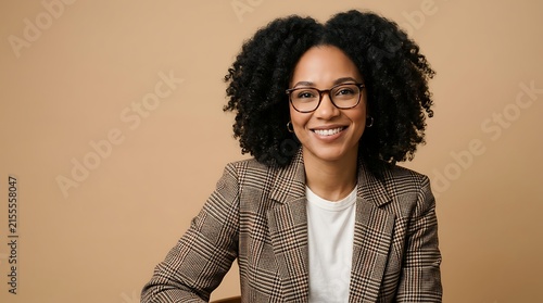 Portrait of a smiling professional woman with curly hair wearing a plaid blazer and glasses