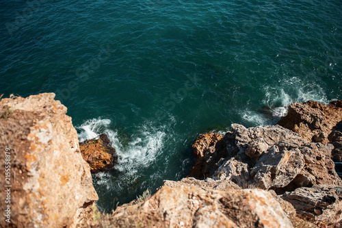 Aerial view of ocean waves crashing against rocky cliffs and large stones