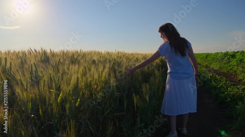 A happy young female teenager walking through a rural countryside path next to a wheat field carrying a bouquet of poppies at sunset