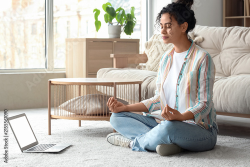 Young African-American woman with laptop meditating at home