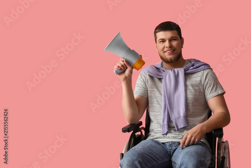 Young man in wheelchair with megaphone on pink background
