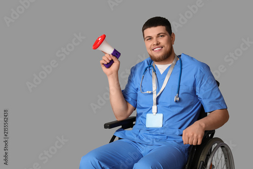 Male doctor in wheelchair with funny megaphone on light background