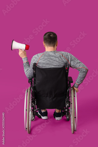 Sporty young man in wheelchair with megaphone on purple background, back view