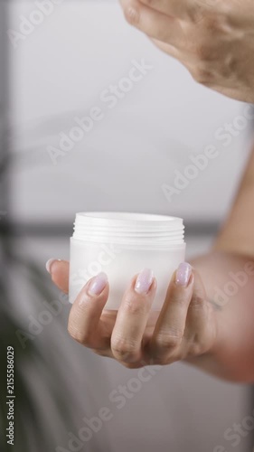 Woman hands holding cosmetic jar and unscrewing lid in close up vertical slow motio