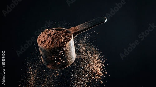 Scoop of Chocolate Protein Powder Scattered on Dark Surface.